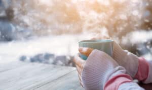 Kobieta ogrzewająca zimne dłonie nad filiżanką gorącej herbaty